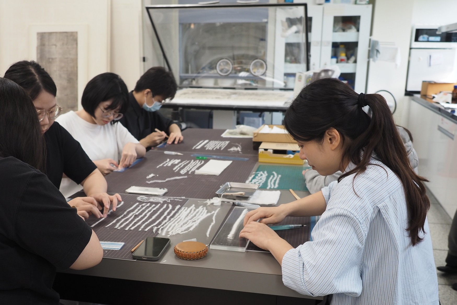 師大文保中心學生們以手工將褚皮紙製作成細長的頂紙，從一般工作桌到實驗用抽風櫃都是他們修護文物的場域。攝影：楊雅棠